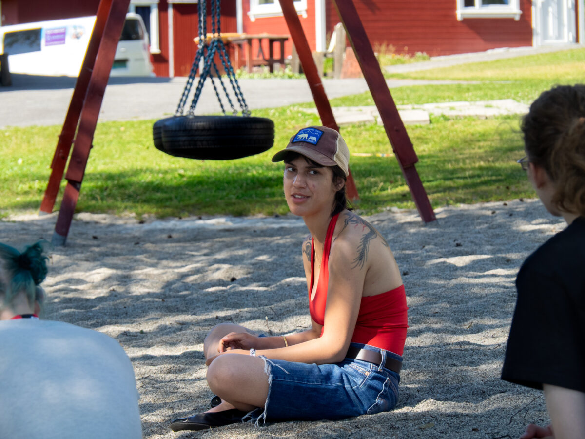 Leiaren for RU, Amrit Kaur, sit på sand. Ho har på ein blå jeans-shorts, og ein raud singlet.