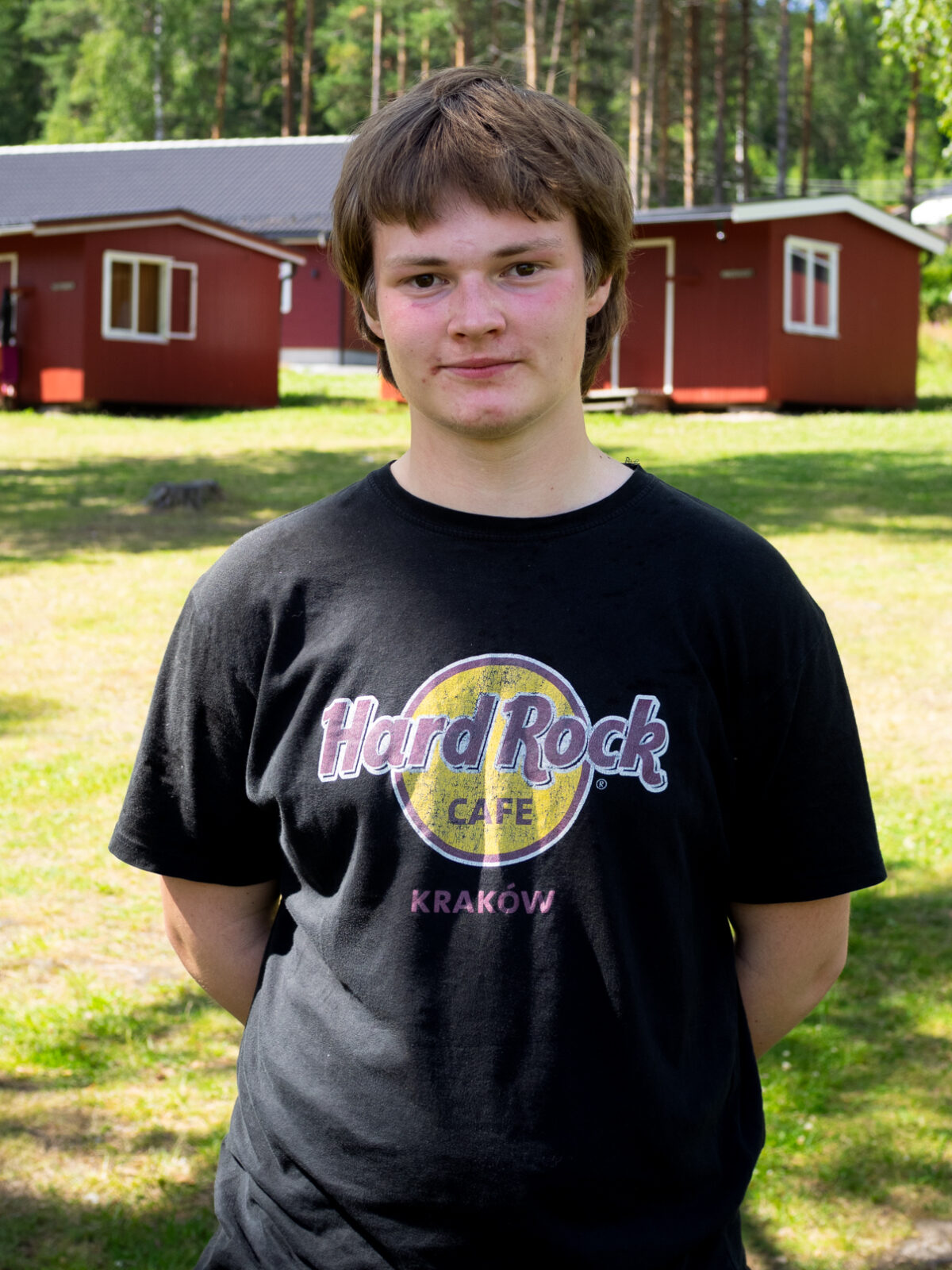 Henning har tjukt brunt hår. Han har på ein tskjorte frå Hard Rock cafe Krakow. Den er sort.